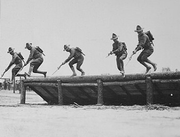 Five soldiers leaping from a log platform during bayonet drill